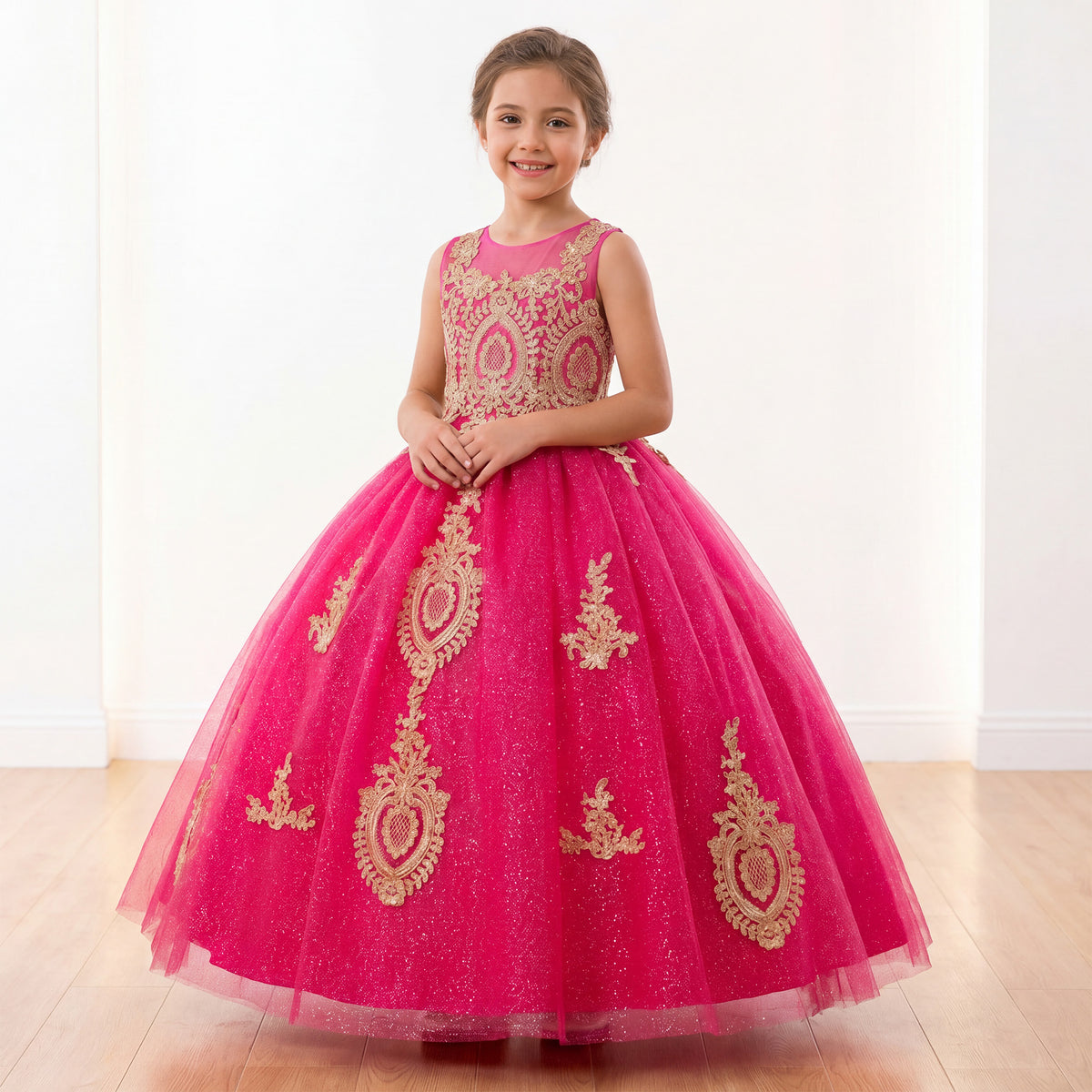 A young girl wearing a bright pink ball gown with gold sequin embroidery, standing in a brightly lit room with white walls and a light wood floor. Main image