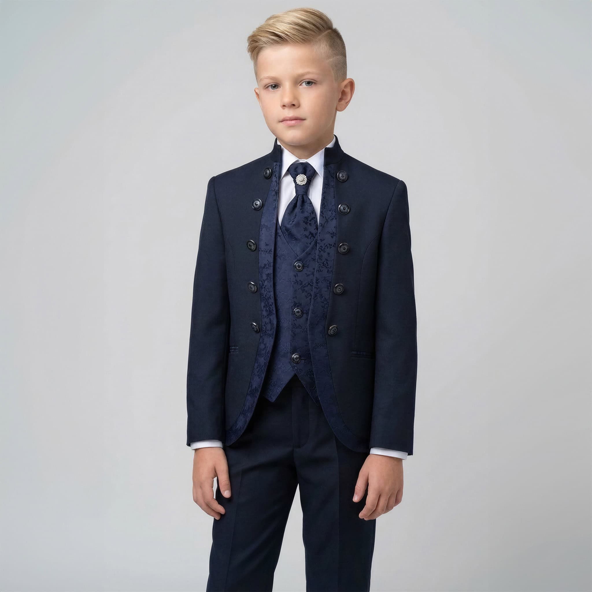 A young boy modeling a formal navy blue three-piece suit with a double-breasted jacket, matching vest, patterned tie, and trousers, set against a plain light gray studio background. Main image
