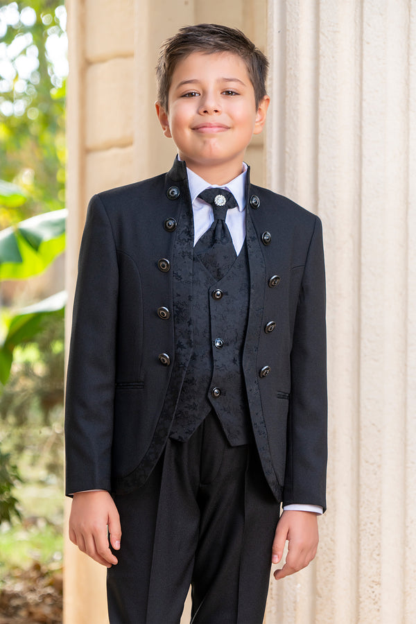 Young boy in a formal black suit standing outdoors with a blurred background