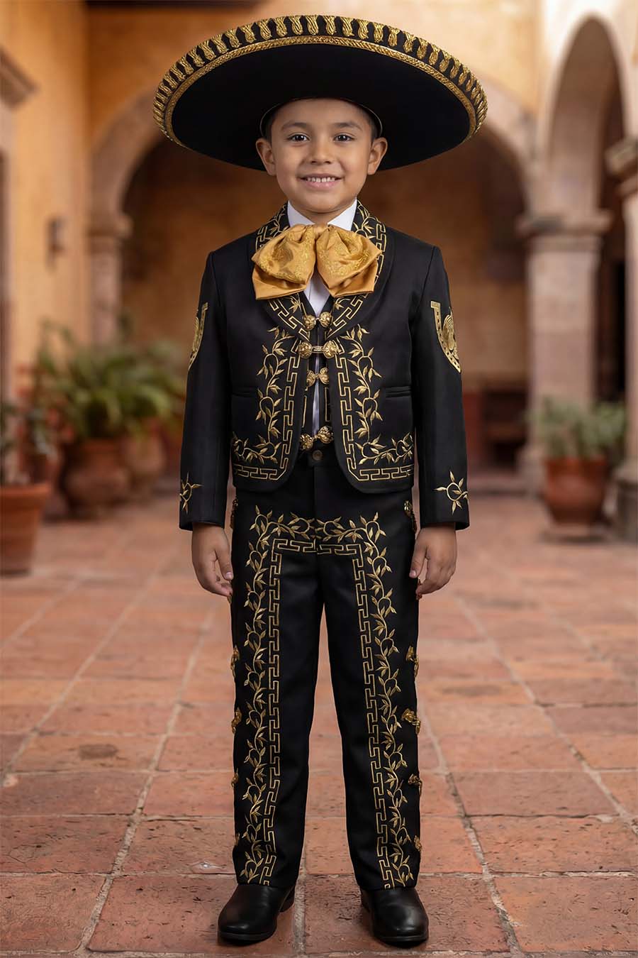 Boy wearing a black and gold charro mariachi suit with gold embroidered horseshoes and horse heads, gold metal buttons, matching sombrero, vest, white shirt, and bow tie.