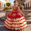 A young girl wearing a traditional Mexican red and cream tulle ball gown stands in front of a stone fountain in a historic town square.