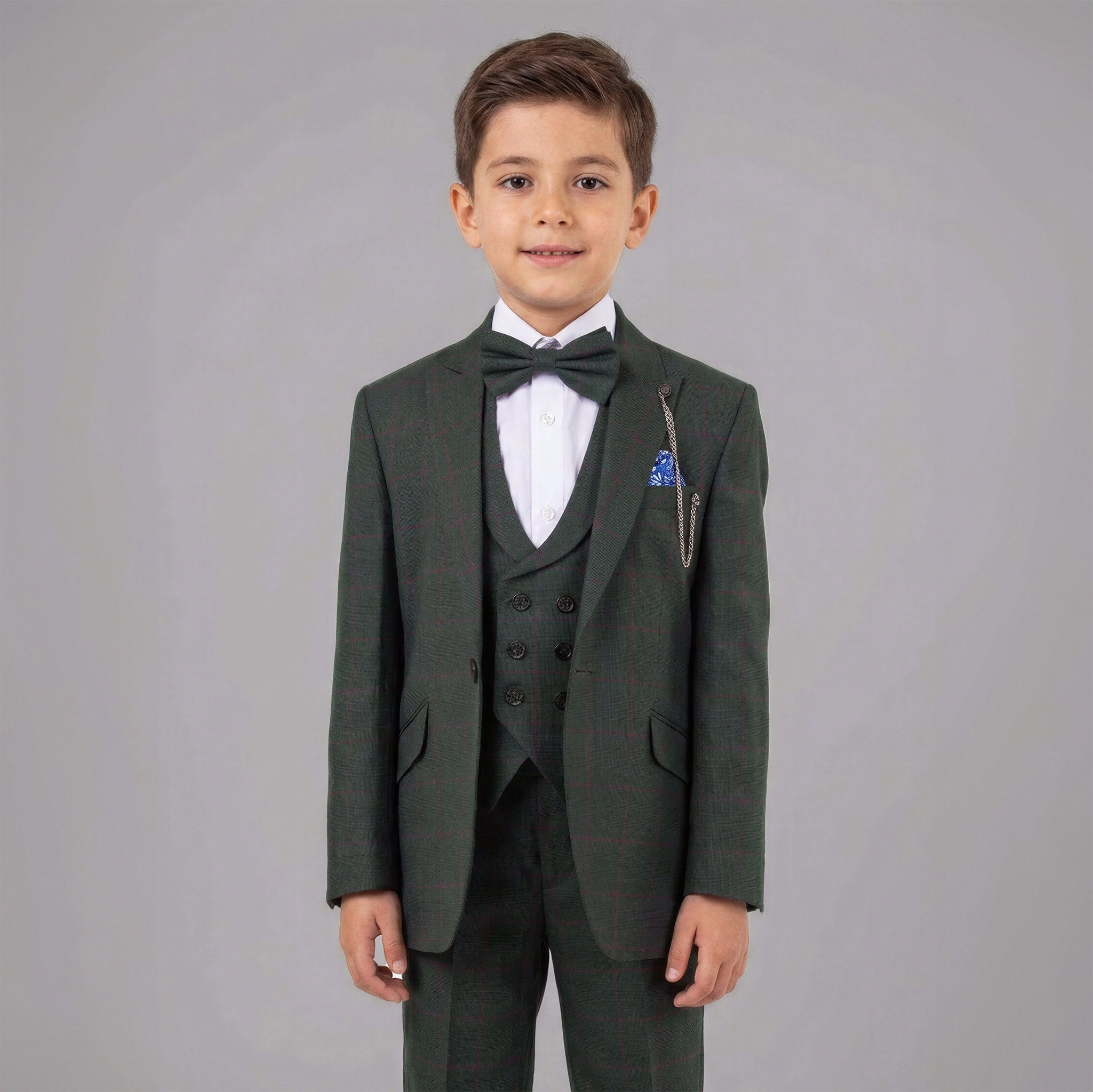 A young boy modeling a dark green three-piece suit with a matching bow tie, white dress shirt, and a blue pocket square against a solid gray studio background. Main image