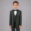 A young boy modeling a dark green three-piece suit with a matching bow tie, white dress shirt, and a blue pocket square against a solid gray studio background.